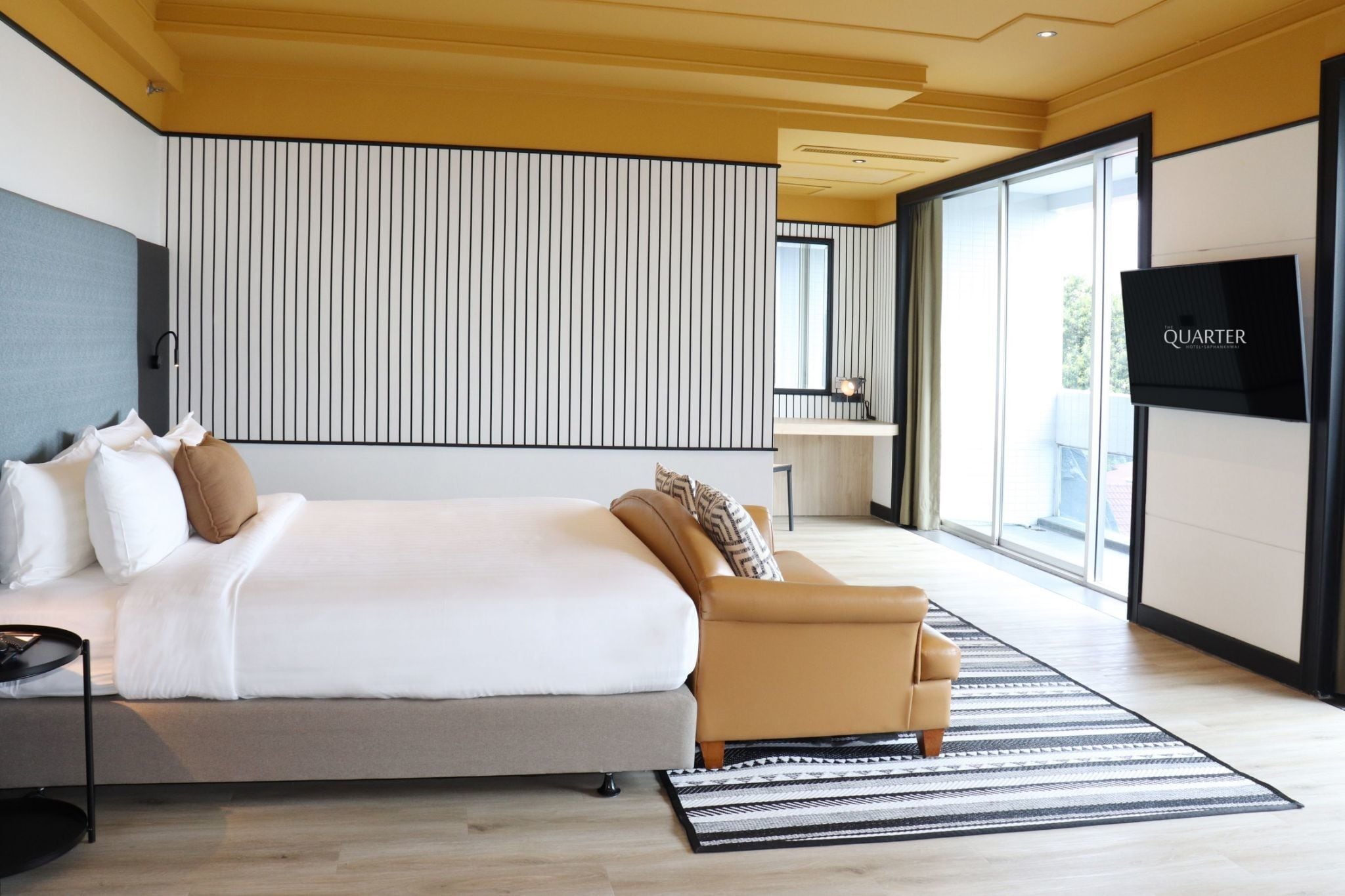 A modern hotel room with a large bed, a sofa, a TV, and a view of the outdoors.