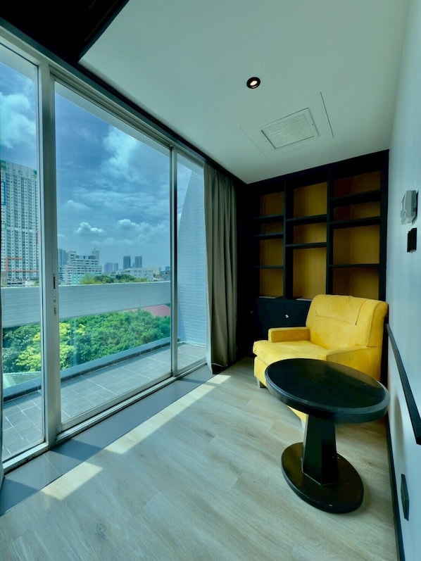 A modern room with a large sliding glass door leading to a balcony, a yellow armchair, a small black table, and a built-in bookshelf. - The Quarter Saphan Khwai by UHG (Bangkok)