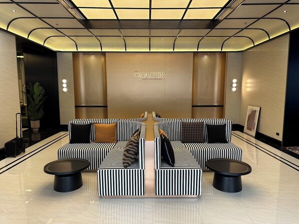Un hall d’hôtel moderne avec un espace salon central agrémenté de canapés à rayures et de tables basses noires.