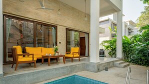 Zona de piscina con sofá y sillones, piscina y una escalera que lleva a un área cubierta.