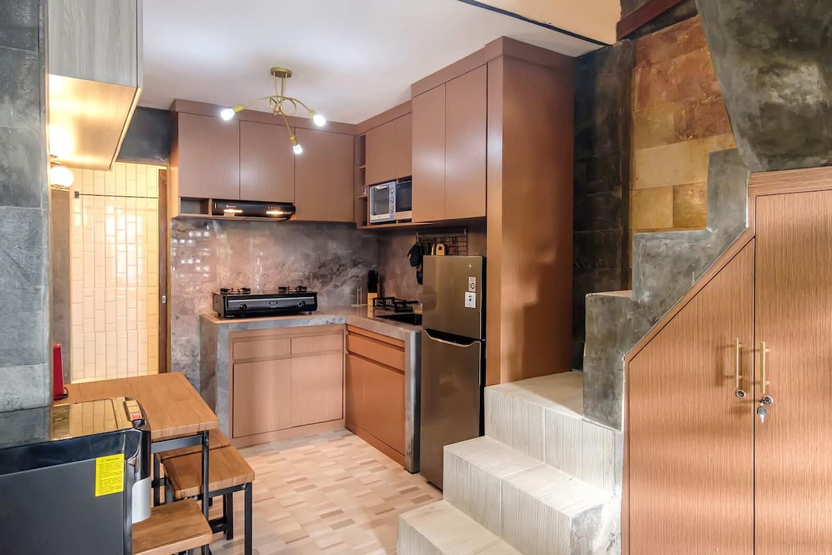 Una cocina moderna con armarios de madera, microondas integrado, refrigerador de acero inoxidable y comedor con mesa y sillas.
