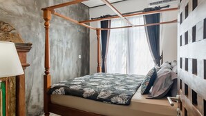 A four-poster bed with a leaf-patterned bedspread, a wooden headboard, and a window with sheer curtains. - Jasmine Villa by TwoSpaces Jimbaran (Jimbaran)