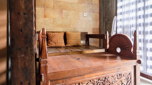 A wooden bed with a headboard, a bench with striped cushions, and a stone wall. - Jasmine Villa by TwoSpaces Jimbaran (Jimbaran)
