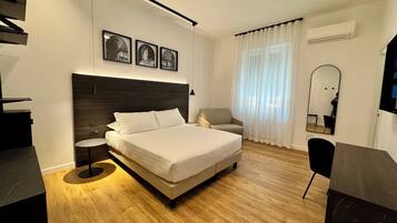 A modern bedroom with a large bed, a small round table, a chair, and a TV.