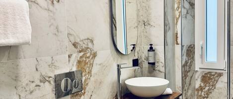 Un baño con pared de mármol, un lavabo, un inodoro, un espejo y una ventana.