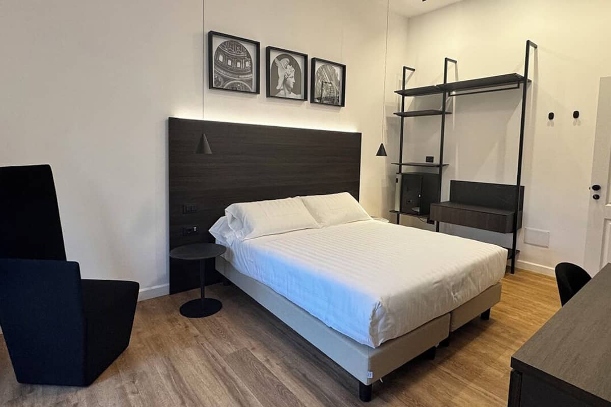 A modern bedroom with a bed, bedside tables, a desk, and a shelving unit.