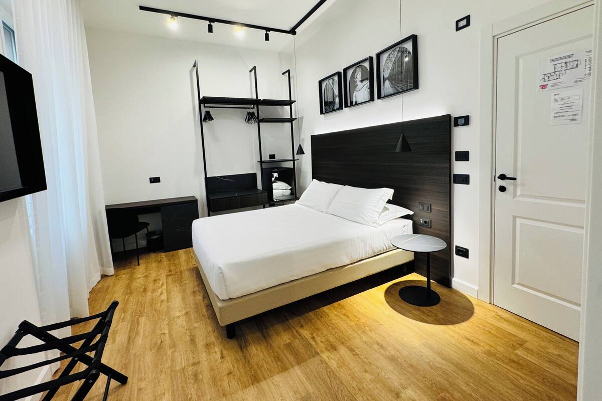 A modern hotel room with a large bed, a desk, a chair, a wardrobe, and a TV.
