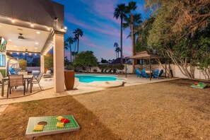 A backyard with a swimming pool, outdoor furniture, and a covered seating area.