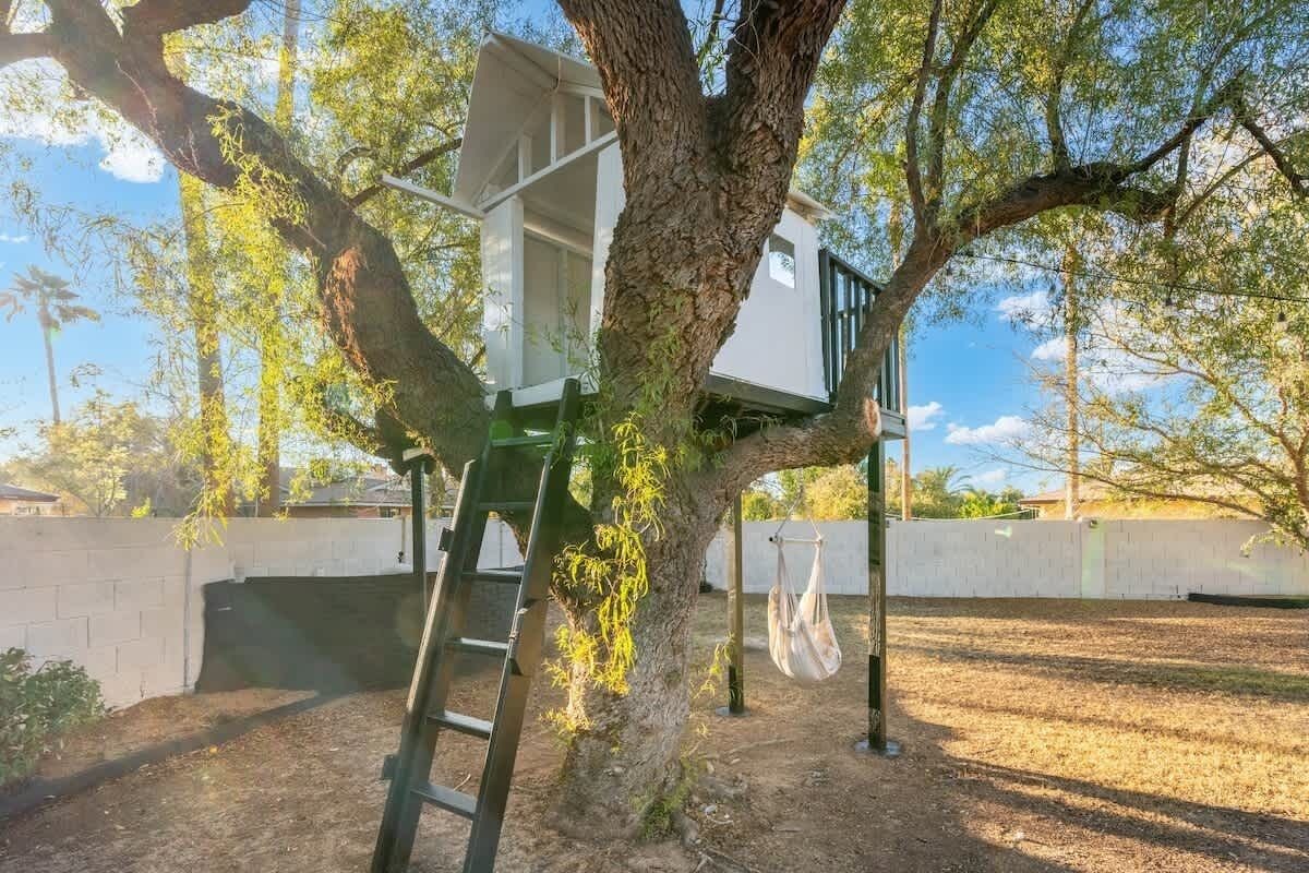 A treehouse attached to a tree, a ladder, and a hanging bag.