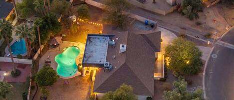 An aerial view of a residential area with a swimming pool, a covered patio, and a street.