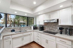 A modern kitchen with white cabinetry, a stainless steel range hood, and a large window providing a view of the outdoors. - SdaleTreehouse|Pool|Gameroom|Firepit (Scottsdale)