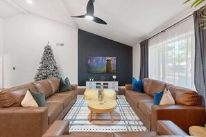 A modern living room with leather sofas, a coffee table, a Christmas tree, and a flat-screen TV mounted on the wall.