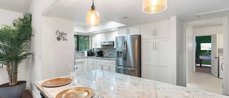 A modern kitchen with white cabinetry, a marble island, and stainless steel appliances.