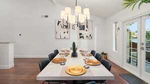 A dining area with a long table set for six, a modern chandelier, and artwork on the walls.