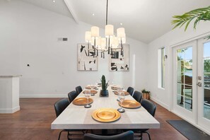 A dining area with a long table set for six, a modern chandelier, and artwork on the walls.