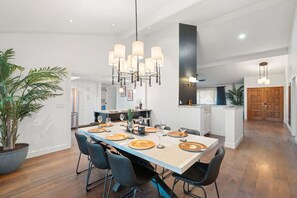 A modern kitchen with a central island, a dining area with a long table set for six, and a large potted plant.