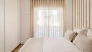 A bedroom with a large bed, a window with sheer curtains, and a striped wall. - Cascais Seacoast Premium Apartment (Cascais)