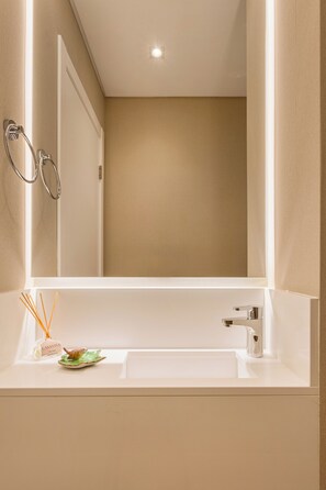 Un baño moderno con lavamanos blanco, un espejo y una zona de ducha.
