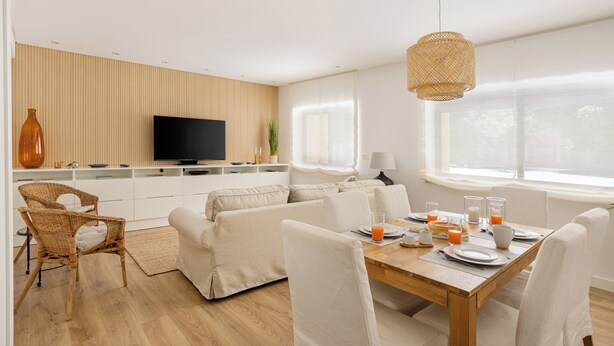 A modern living room with a sofa, dining table, and chairs. There is a television, a vase, and a window with curtains. - Cascais Seacoast Premium Apartment (Cascais)