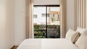 A bedroom with a bed, curtains, and a view of an outdoor balcony with a table and chairs. - Cascais Seacoast Premium Apartment (Cascais)