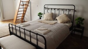 A neatly made bed with a metal frame, a bedside table with a plant, and a wooden ladder against the wall. - Luxury Prague Apartment in Heart of City (Prague)