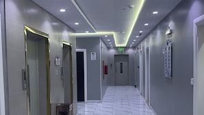 Een moderne hotelgang met marmeren vloer, meerdere deuren en inbouwspots.