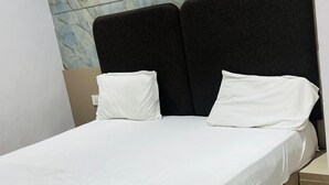 A bed with a white mattress and two pillows, a dark headboard, and a marble-patterned wall behind it. - Hotel Shree Radham By GRB (Mathura)