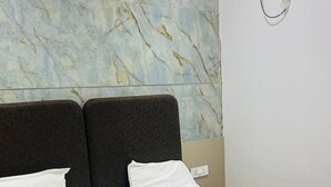 A modern hotel room with a marble-patterned wall, a large bed with white linens, and a wall-mounted air conditioning unit. - Hotel Shree Radham By GRB (Mathura)