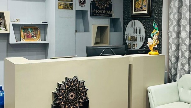 A reception area with a reception desk, a waiting area with a chair, and a wall-mounted air conditioner. - Hotel Shree Radham By GRB (Mathura)