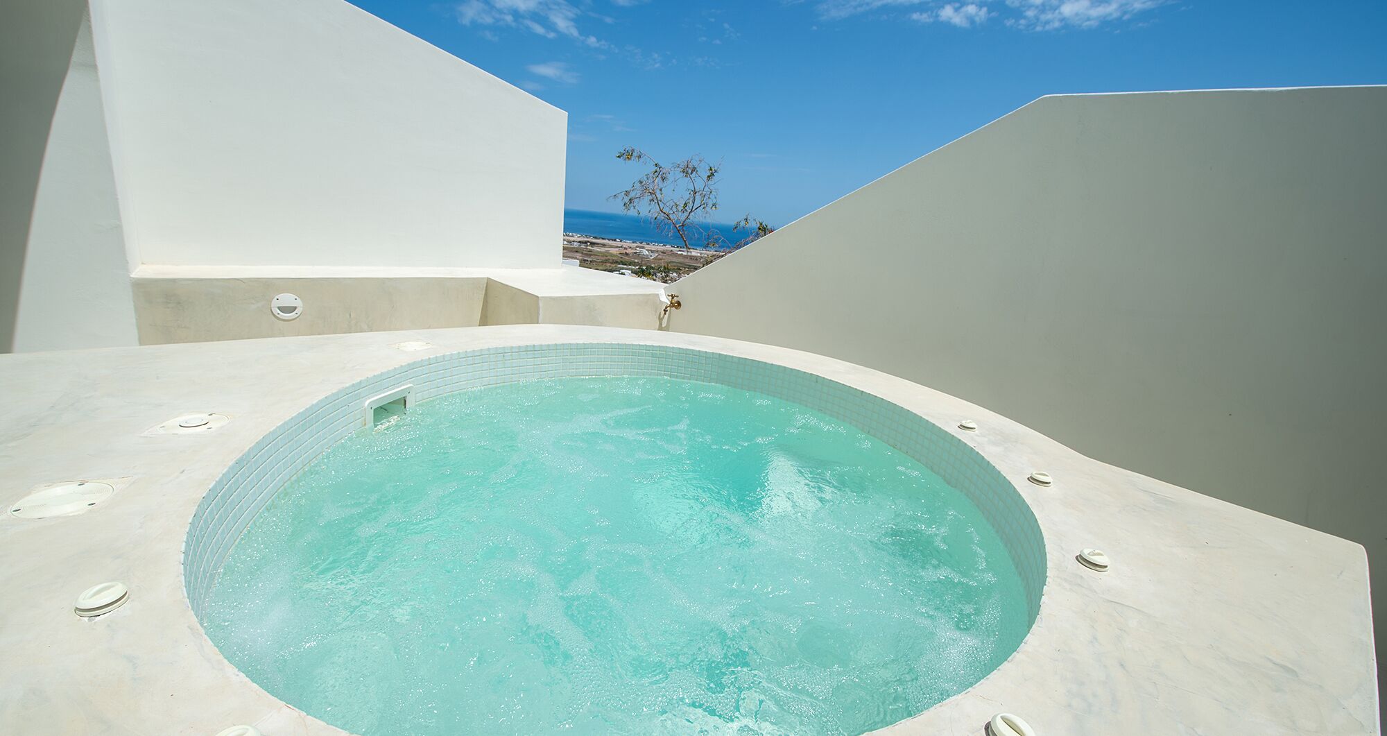 Un moderno jacuzzi al aire libre con vistas despejadas al mar y un árbol de fondo.