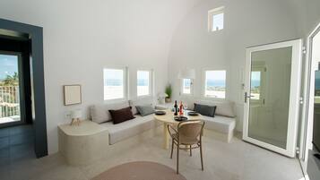Una sala de estar moderna con un sofá, una mesa de comedor y una silla. Varias ventanas ofrecen vistas al exterior.