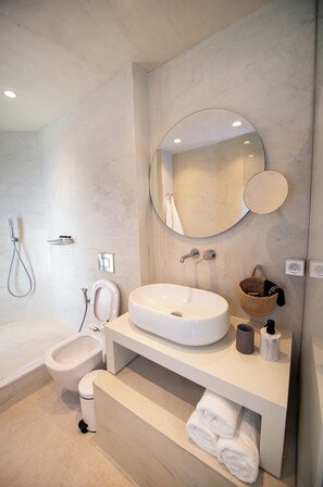 A modern bathroom with a freestanding bathtub, a round mirror, a sink, and a bidet.