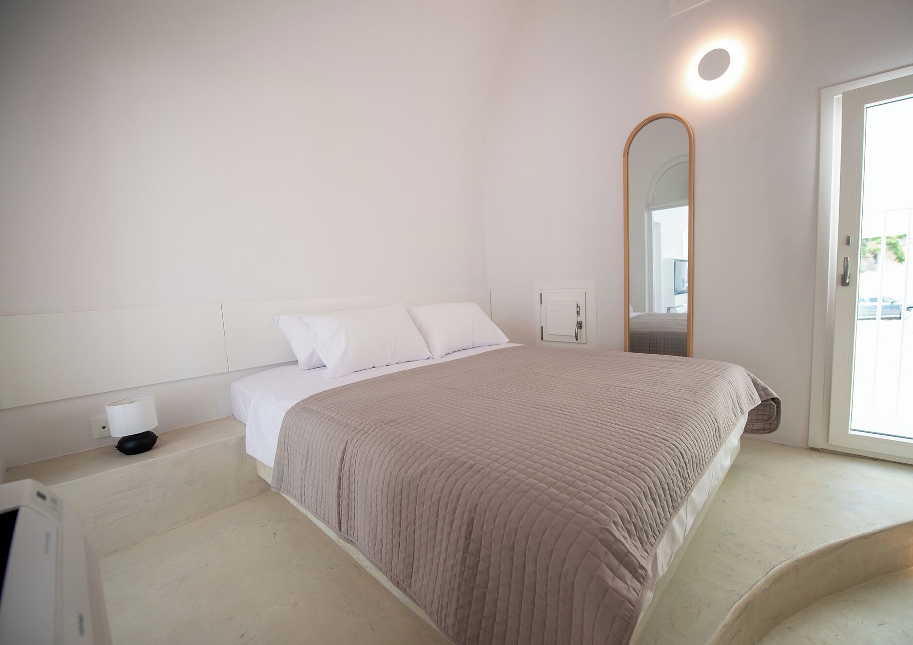 A bedroom with a bed, a bedside table, a mirror, and a window.