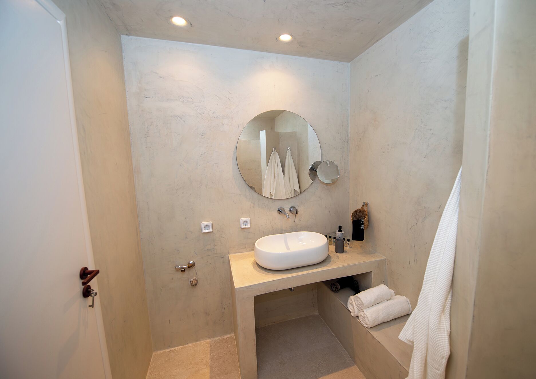A bathroom with a round mirror, a sink, and a towel rack.