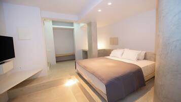 Quarto de hotel moderno com cama, televisão, guarda-roupa e banheiro visível por uma porta aberta.