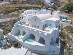 A white building with multiple balconies, a swimming pool, and a parking area.