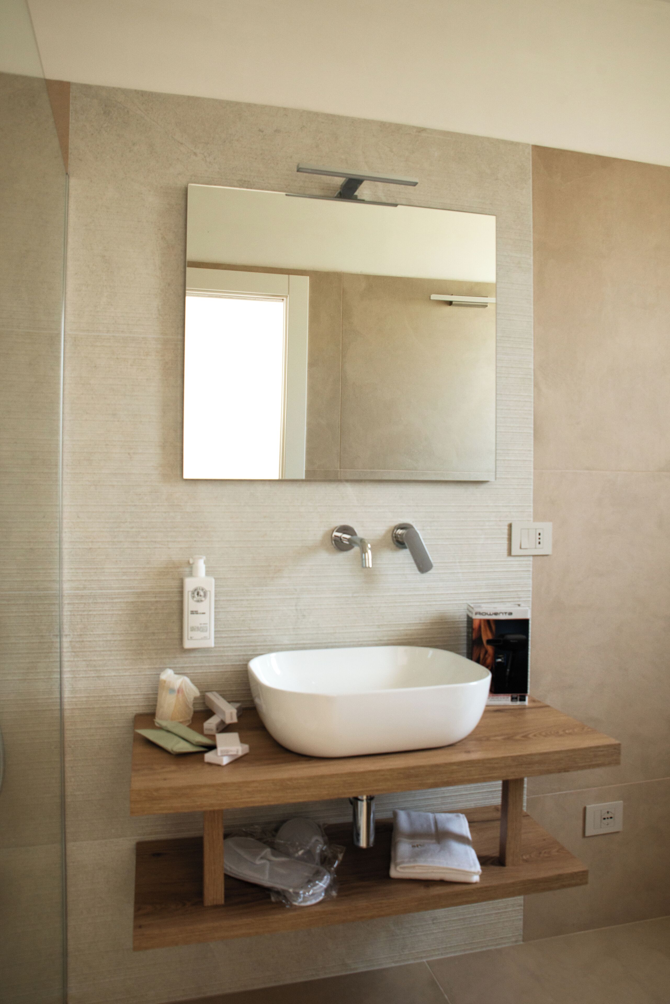 A modern bathroom with a large white sink, a mirror above it, and a wooden vanity.