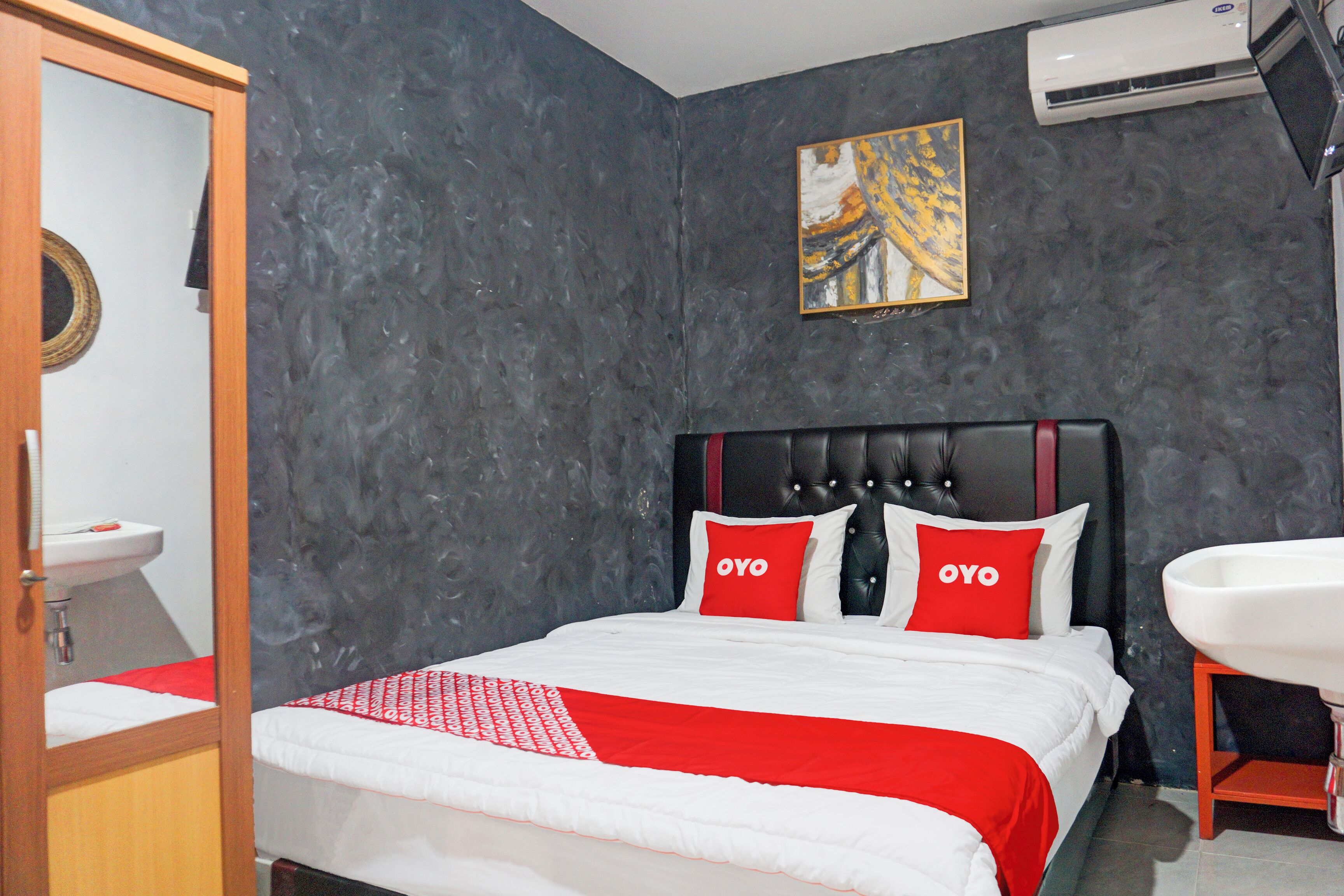 Una habitación de hotel con una cama, una colcha roja y blanca, un cabecero negro y un cuadro en la pared.