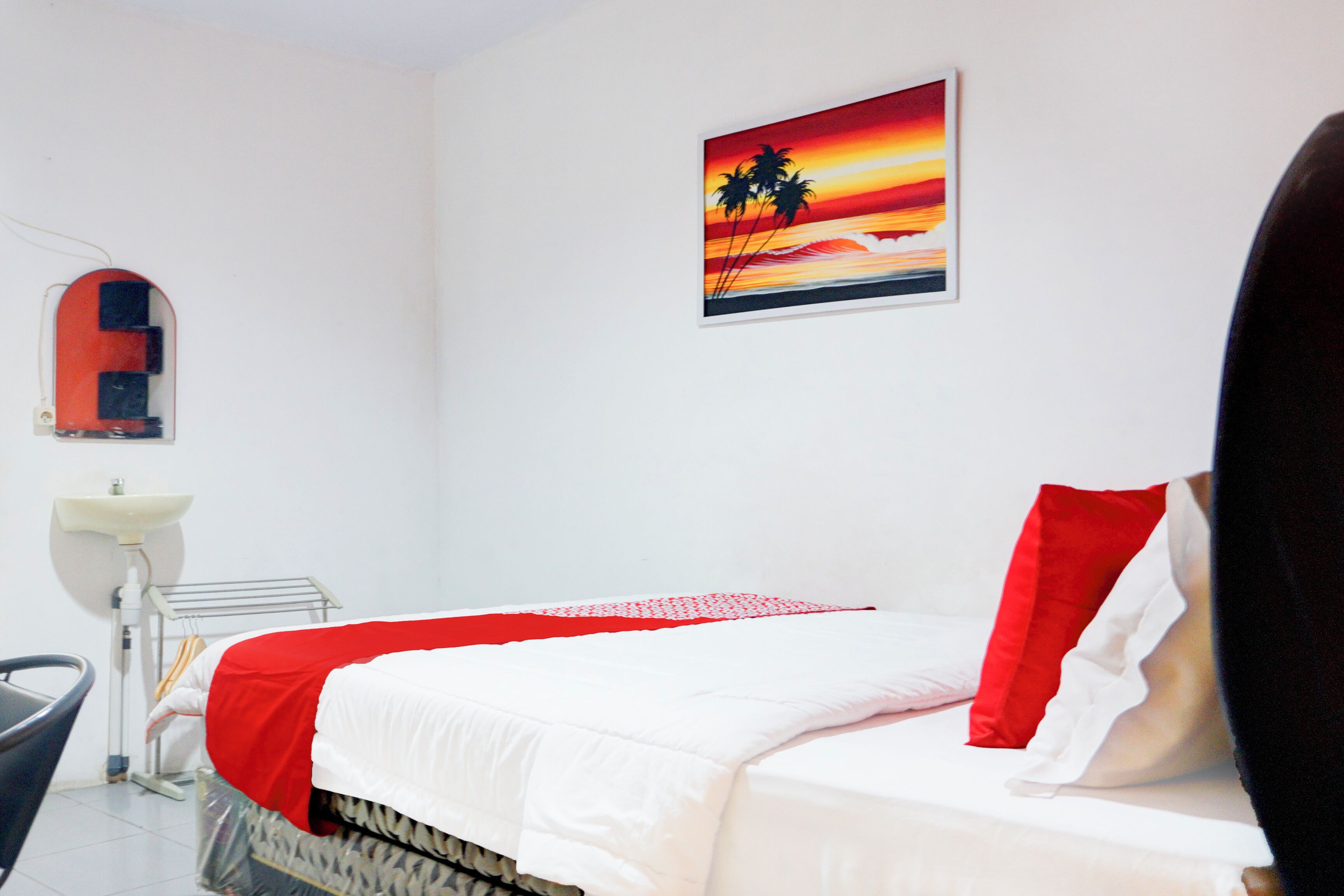 A hotel room with a bed, a painting of a sunset, a sink, and a chair.