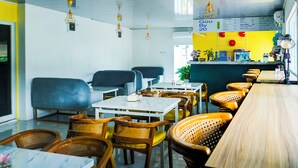A restaurant with a yellow and white color scheme, featuring tables and chairs, hanging lights, and a menu board. - Hotel O Bandar Lampung Near Gor Saburai Formerly Omah Anakku (Bandar Lampung)