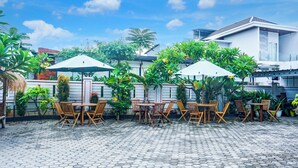 A courtyard with hexagonal paving, wooden tables and chairs, and umbrellas. - Hotel O Bandar Lampung Near Gor Saburai Formerly Omah Anakku (Bandar Lampung)
