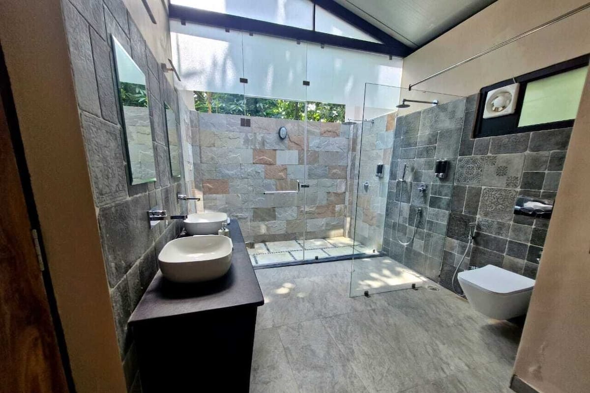 Een moderne badkamer met een stenen muur, een glazen douchecabine, een wastafel en een toilet.