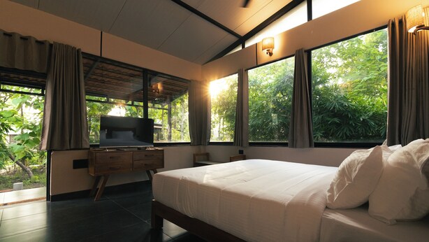 Ein Schlafzimmer mit einem großen Bett, einem Nachttisch aus Holz, einem Fernseher und einem Fenster mit Vorhängen.