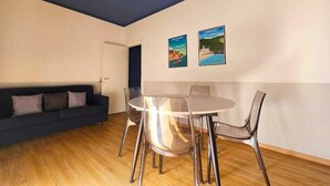 Una habitación con una mesa redonda de vidrio, cuatro sillas, un sofá azul oscuro y dos carteles en la pared.