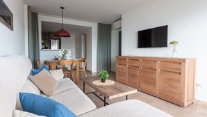 Een moderne woonkamer met een bank, een houten salontafel en een aan de muur bevestigde televisie.