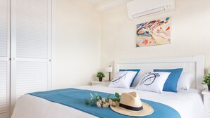 Een net opgemaakt bed met een blauw laken, een strohoed en een bloemstuk.