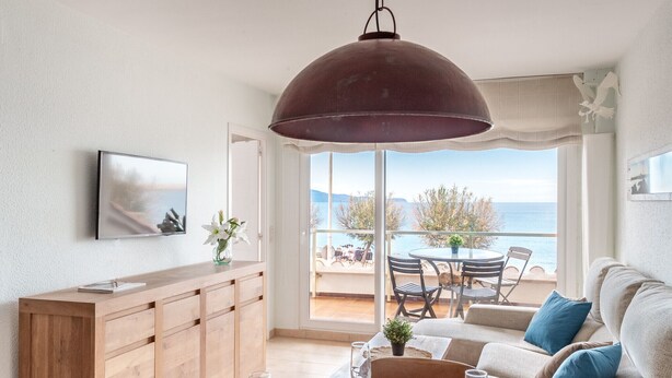 Een moderne woonkamer met een houten kast, een eettafel voor twee personen en een groot raam met uitzicht op de zee.