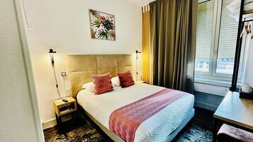 Une chambre d’hôtel comprenant un lit, une table de chevet, une commode, une fenêtre avec des rideaux et une œuvre d’art accrochée au mur.