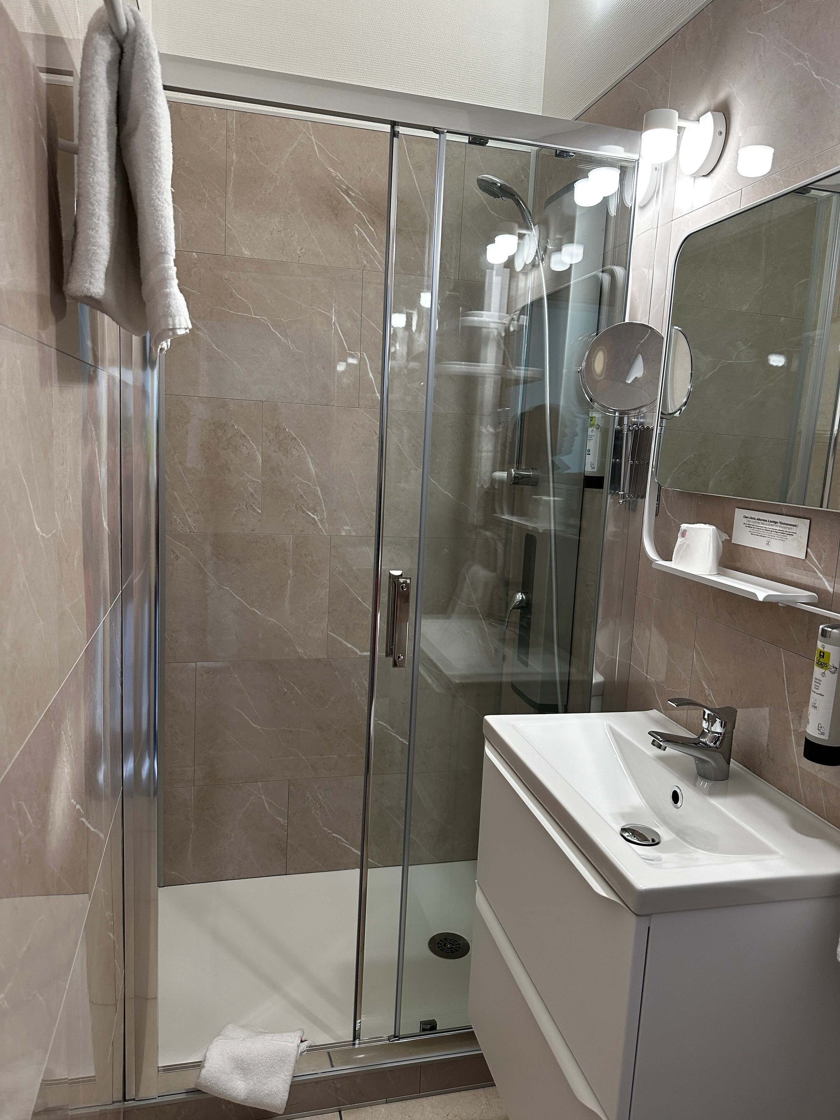 Une salle de bain moderne avec une douche à parois de verre, un lavabo blanc et un miroir.