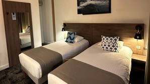 A hotel room with two beds, a mounted TV, a door, and a mirror. - Logis Hôtel le Passiflore (Chateaubernard)